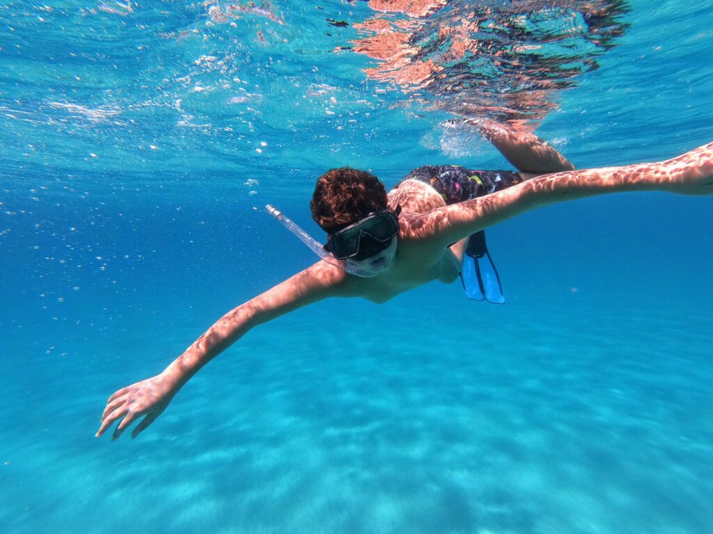 Underwater view of a snorkeler gliding through the vibrant blue sea at Mari Pintau.
