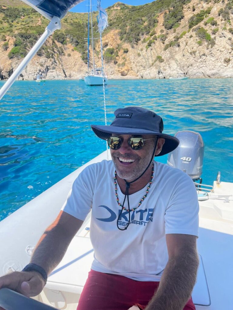 Photograph of Mauro Tedesco, a skipper, smiling while at the helm of a boat in a sunny coastal location